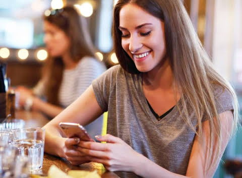 A woman writing an online review on her phone about her recent dining experience after scanning a QR code on the table